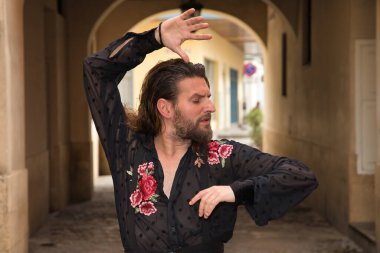 Sakallı, uzun saçlı, siyah şeffaf gömlekli, siyah puantiyeli, kırmızı güllü, siyah pantolonlu ve ceketli, şehirde flamenko dansı yapan genç bir adam. Sanat, dans, kültür, gelenek.