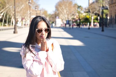 Pembe ceketli, güneş gözlüklü, avuç içleri dua eden güzel bir Güney Amerikalı kadın. Dini, duayı, katoliği, inancı kavra.