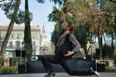 Sakallı, at kuyruklu, siyah tişörtlü, beyaz benekli, siyah pantolonlu ve ceketli, sahnede şapkalı flamenko dansı yapan genç bir adam. Sanat, dans, kültür, gelenek.