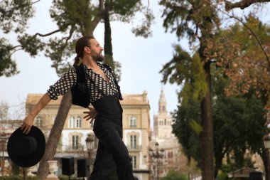 Sakallı, at kuyruklu, siyah tişörtlü, beyaz benekli, siyah pantolonlu ve ceketli, sahnede şapkalı flamenko dansı yapan genç bir adam. Sanat, dans, kültür, gelenek.