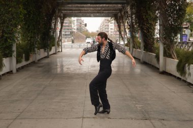 Sakallı, at kuyruklu, siyah tişörtlü, beyaz benekli, siyah pantolonlu ve ceketli, şehrin ortasında flamenko dansı yapan genç bir adam. Sanat, dans, kültür, gelenek.