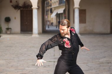 Sakallı, at kuyruklu, siyah şeffaf gömlekli, siyah puantiyeli, kırmızı güllü, siyah pantolonlu ve ceketli, şehirde flamenko dansı yapan genç bir adam. Sanat, dans, kültür, gelenek.