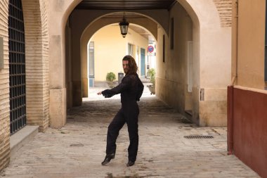 Sakallı ve uzun saçlı siyah şeffaf gömlekli siyah puantiyeli, siyah pantolonlu ve ceketli şehirde flamenko dansı yapan genç bir adam. Sanat, dans, kültür, gelenek.