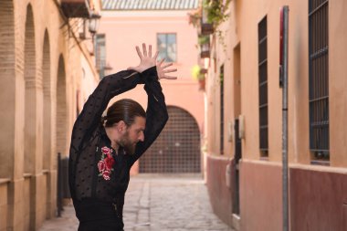 Sakallı, at kuyruklu, siyah şeffaf gömlekli, siyah puantiyeli, kırmızı güllü, siyah pantolonlu ve ceketli, şehirde flamenko dansı yapan genç bir adam. Sanat, dans, kültür, gelenek.