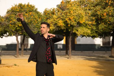 Siyah gömlekli, ceketli ve pantolonlu, kırmızı noktalı siyah mendilli, kastanyetli, sokakta flamenko dansı yapan genç bir İspanyol. Sanat, dans, kültür, gelenek.