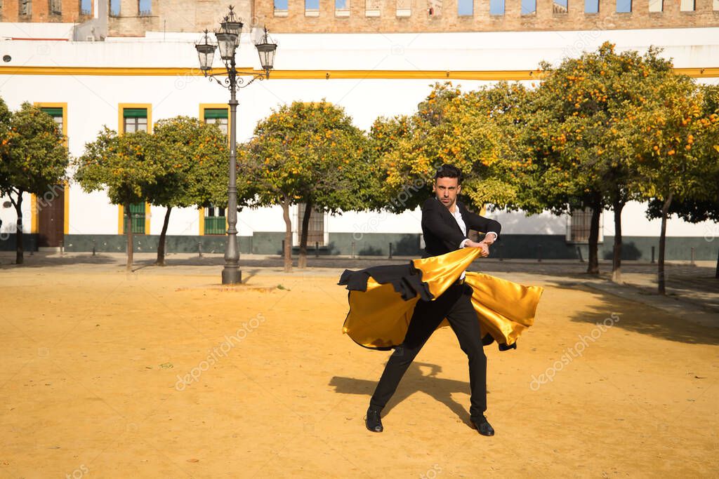 Young Spanish man in black shirt, jacket and pants, with dancing shoes, dancing flamenco with black and gold capote in the street. Typical Spanish concept, art, dance, culture, tradition.