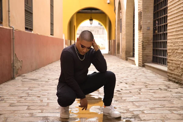 İkili olmayan, genç ve Güney Amerikalı, sokağın ortasında ağır makyajlı, elleri başının üstünde, su birikintisindeki yansımasına endişeyle bakıyor. Kavram kraliçesi, lgbtq +, gurur, nonoş.