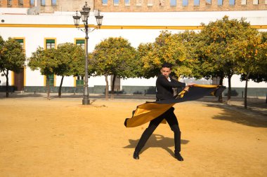 Siyah gömlekli, ceketli ve pantolonlu, dans ayakkabılı, siyah ve altın pelerinli, flamenko dansı yapan genç bir İspanyol. Tipik İspanyol konsepti, sanat, dans, kültür, gelenek.