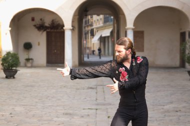 Sakallı, at kuyruklu, siyah şeffaf gömlekli, siyah puantiyeli, kırmızı güllü, siyah pantolonlu ve ceketli, şehirde flamenko dansı yapan genç bir adam. Sanat, dans, kültür, gelenek.
