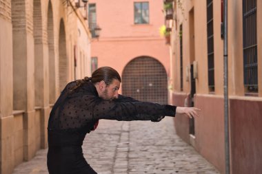 Sakallı, at kuyruklu, siyah şeffaf gömlekli, siyah benekli, siyah pantolonlu ve ceketli, şehirde flamenko dansı yapan genç bir adam. Sanat, dans, kültür, gelenek.