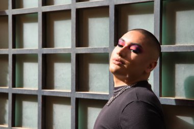 İkili olmayan, genç ve Güney Amerikalı portresi, ağır bir şekilde yarı açık gözlerle yapılmış, güneş ışınları alıyor. Kavram kraliçesi, lgbtq +, gurur, nonoş.