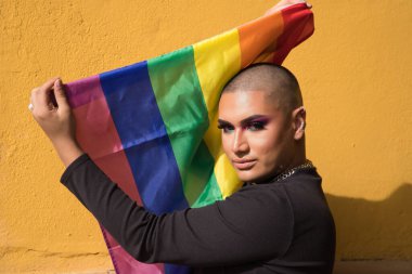 İkili olmayanların portresi, genç ve Güney Amerikalı, aşırı makyajlı ve şehvetli bir şekilde eşcinsel gurur bayrağı taşıyor. Kavram kraliçesi, lgbtq +, gurur, nonoş.