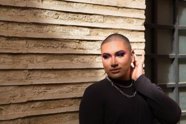 İkili olmayan birinin portresi, genç ve Güney Amerikalı, ağır ağır tuğla bir duvarda, güneş ışınları alıyor. Kavram kraliçesi, lgbtq +, gurur, nonoş.