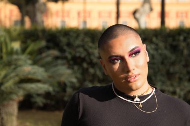 İkili olmayan bir kişinin portresi, genç ve Güney Amerikalı, makyajlı, yüzüne güneş ışınları geliyor. Kavram kraliçesi, lgbtq +, gurur, nonoş.