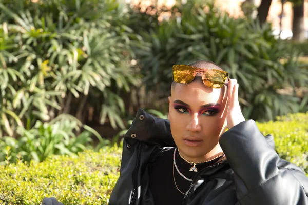 İkili olmayan genç ve Güney Amerikalı birinin portresi. Makyajlı ve kafasında aynalı güneş gözlüğü var. Etrafı yeşillikle çevrili. Kavram kraliçesi, lgbtq +, gurur, nonoş.