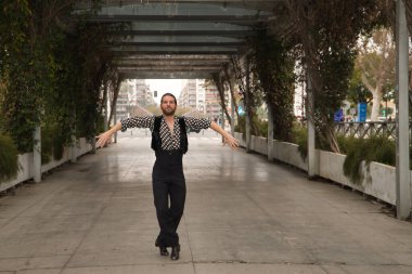 Sakallı, at kuyruklu, siyah tişörtlü, beyaz benekli, siyah pantolonlu ve ceketli, şehrin ortasında flamenko dansı yapan genç bir adam. Sanat, dans, kültür, gelenek.