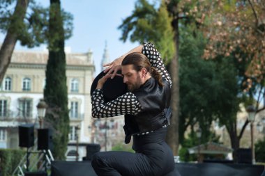 Sakallı, at kuyruklu, siyah tişörtlü, beyaz benekli, siyah pantolonlu ve ceketli, sahnede şapkalı flamenko dansı yapan genç bir adam. Sanat, dans, kültür, gelenek.