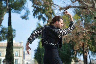 Sakallı, at kuyruklu, siyah tişörtlü, beyaz benekli, siyah pantolonlu ve ceketli, sahnede flamenko dansı yapan genç bir adam. Sanat, dans, kültür, gelenek.