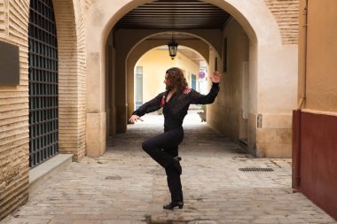 Sakallı, uzun saçlı, siyah şeffaf gömlekli, siyah puantiyeli, kırmızı güllü, siyah pantolonlu ve ceketli, şehirde flamenko dansı yapan genç bir adam. Sanat, dans, kültür, gelenek.