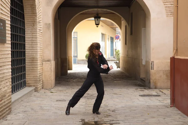 Sakallı, uzun saçlı, siyah şeffaf gömlekli, siyah puantiyeli, kırmızı güllü, siyah pantolonlu ve ceketli, şehirde flamenko dansı yapan genç bir adam. Sanat, dans, kültür, gelenek.