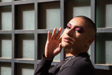 İkili olmayan bir kişinin portresi, genç ve Güney Amerikalı, yüzünde ağır bir el ile makyaj yapıyor, güneş ışınlarını alıyor. Kavram kraliçesi, lgbtq +, gurur, nonoş.