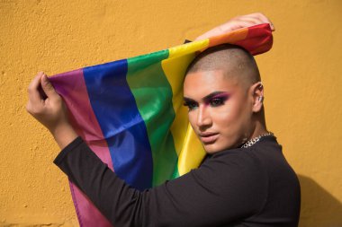 İkili olmayanların portresi, genç ve Güney Amerikalı, aşırı makyajlı ve şehvetli bir şekilde eşcinsel gurur bayrağı taşıyor. Kavram kraliçesi, lgbtq +, gurur, nonoş.