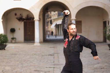 Sakallı, at kuyruklu, siyah şeffaf gömlekli, siyah puantiyeli, kırmızı güllü, siyah pantolonlu ve ceketli, şehirde flamenko dansı yapan genç bir adam. Sanat, dans, kültür, gelenek.