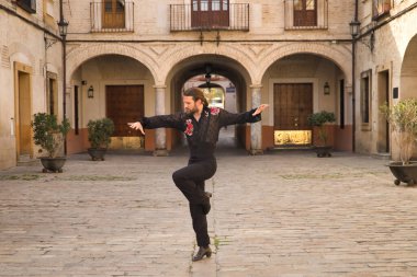 Sakallı, at kuyruklu, siyah şeffaf gömlekli, siyah puantiyeli, kırmızı güllü, siyah pantolonlu ve ceketli, şehirde flamenko dansı yapan genç bir adam. Sanat, dans, kültür, gelenek.