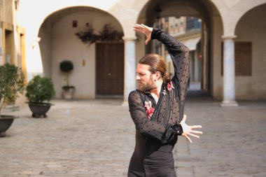 Sakallı, at kuyruklu, siyah şeffaf gömlekli, siyah puantiyeli, kırmızı güllü, siyah pantolonlu ve ceketli, şehirde flamenko dansı yapan genç bir adam. Sanat, dans, kültür, gelenek.