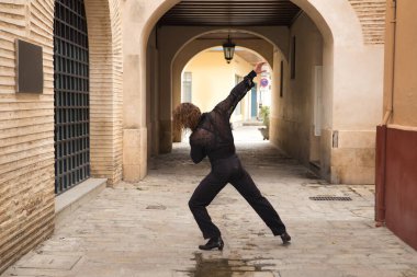 Sakallı ve uzun saçlı siyah şeffaf gömlekli siyah puantiyeli, siyah pantolonlu ve ceketli şehirde flamenko dansı yapan genç bir adam. Sanat, dans, kültür, gelenek.