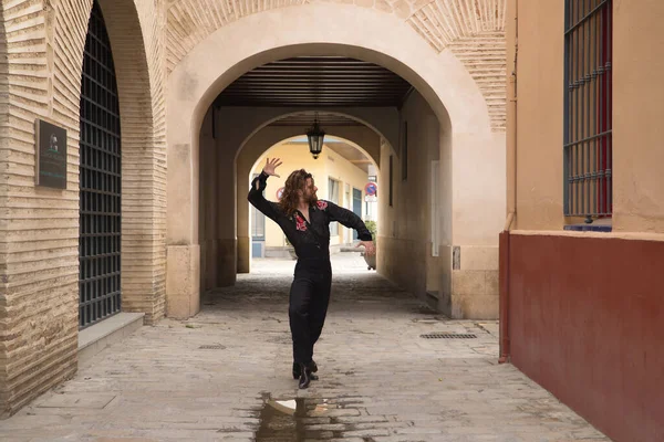 Sakallı, uzun saçlı, siyah şeffaf gömlekli, siyah puantiyeli, kırmızı güllü, siyah pantolonlu ve ceketli, şehirde flamenko dansı yapan genç bir adam. Sanat, dans, kültür, gelenek.