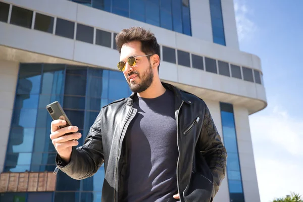 Sakallı, güneş gözlüklü, deri ceketli, cep telefonundan sosyal ağları kontrol eden yakışıklı bir genç. Güzelliği, modayı, eğilimi, uygulamayı, akıllı telefonu, sosyal ağları kavra.