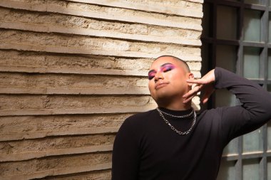 İkili olmayan, genç ve Güney Amerikalı birinin portresi, gözleri tuğla bir duvarda kapalı, güneş ışınları alıyor. Kavram kraliçesi, lgbtq +, gurur, nonoş.