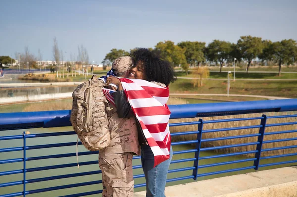 African American woman with American flag embracing her partner, an American soldier who has just arrived from a mission. Concept army, missions, military, war, love, hugs.