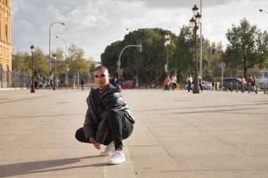 İkili olmayan, genç ve Güney Amerikalı, aşırı makyajlı, tamamen siyah giyinmiş, Avrupa 'da tatilde çömelmiş poz veriyor. Kavram kraliçesi, lgbtq +, gurur, nonoş.