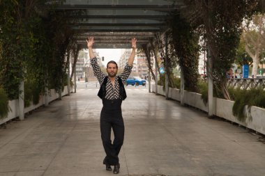 Sakallı, at kuyruklu, siyah tişörtlü, beyaz benekli, siyah pantolonlu ve ceketli, şehrin ortasında flamenko dansı yapan genç bir adam. Sanat, dans, kültür, gelenek.