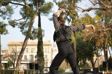 Sakallı, at kuyruklu, siyah tişörtlü, beyaz benekli, siyah pantolonlu ve ceketli, sahnede flamenko dansı yapan genç bir adam. Sanat, dans, kültür, gelenek.