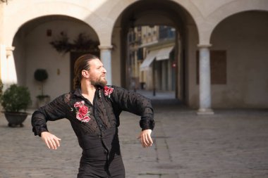 Sakallı, at kuyruklu, siyah şeffaf gömlekli, siyah puantiyeli, kırmızı güllü, siyah pantolonlu ve ceketli, şehirde flamenko dansı yapan genç bir adam. Sanat, dans, kültür, gelenek.