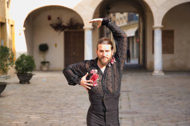 Sakallı, at kuyruklu, siyah şeffaf gömlekli, siyah puantiyeli, kırmızı güllü, siyah pantolonlu ve ceketli, şehirde flamenko dansı yapan genç bir adam. Sanat, dans, kültür, gelenek.