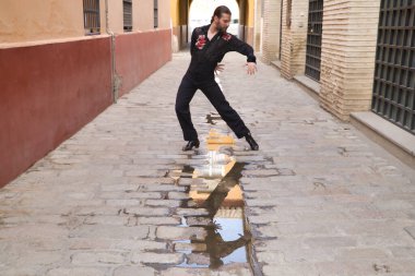 Sakallı ve uzun saçlı, siyah şeffaf gömlekli, siyah puantiyeli, kırmızı güllü, siyah pantolonlu ve ceketli, su birikintisinde yansıması olan flamenko dansı yapan genç bir adam. Sanat kavramı, dans..