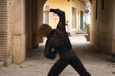 Sakallı ve uzun saçlı siyah şeffaf gömlekli siyah puantiyeli, siyah pantolonlu ve ceketli şehirde flamenko dansı yapan genç bir adam. Sanat, dans, kültür, gelenek.