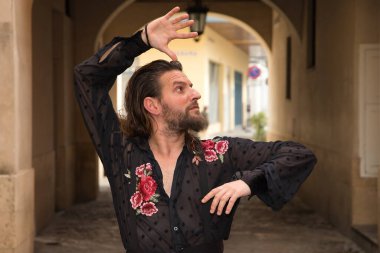 Sakallı, uzun saçlı, siyah şeffaf gömlekli, siyah puantiyeli, kırmızı güllü, siyah pantolonlu ve ceketli, şehirde flamenko dansı yapan genç bir adam. Sanat, dans, kültür, gelenek.