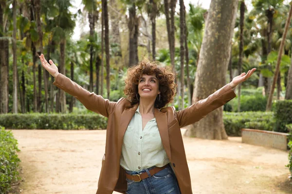 Mature and attractive woman, independent, successful, empowered with brown leather jacket and jeans with open arms giving thanks to life very happy. Concept happiness, triumph, empowerment.