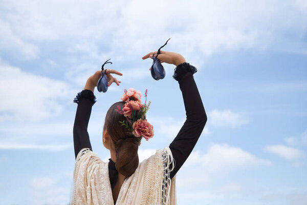 Portrait of young teenage girl in black dance dress, white shawl and pink carnations in her hair, dancing flamenco with castanets in her hands. Concept of flamenco, dance, art, typical Spanish dance.