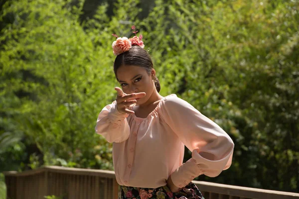 Portrait of young teenage woman in pink shirt, black skirt with flowers and pink carnations in her hair, dancing flamenco on wooden bridge. Flamenco concept, dance, art, typical Spanish dance.