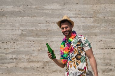 Genç ve yakışıklı bir adam, mavi gözlü, mükemmel gülüşlü, sakallı, şapkalı, Hawaii gömlekli ve elinde gri bir arka planda bira şişesi olan çiçek kolyeli. Tatiller, partiler, geziler, içkiler.