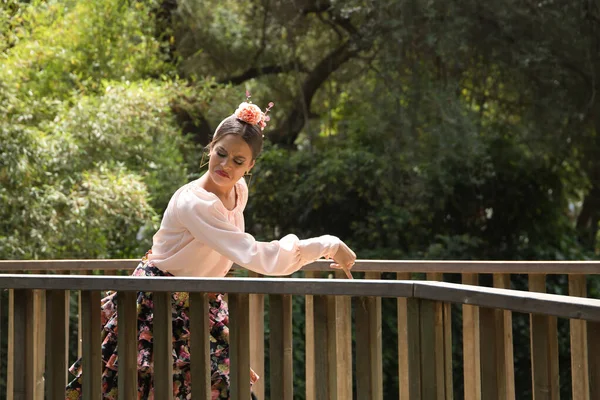 Young teenage woman in pink shirt, black skirt with flowers and pink carnations in her hair, dancing flamenco on wooden bridge. Flamenco concept, dance, art, typical Spanish dance.