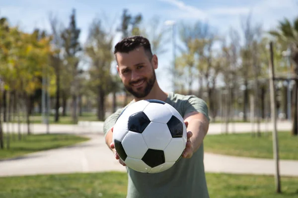 Young and handsome man, with a beard and green shirt, with blue eyes, perfect smile, offering a soccer ball, smiling. Concept sport, ball, football, world, competition. Selective focus on ball.