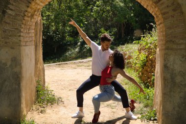 Çekici genç bir çift, açık hava parkında antik bir taş kemerin altında şehvetli bir şekilde dans ediyor. Latince, şehvetli, folklorik, şehir dansı konsepti.