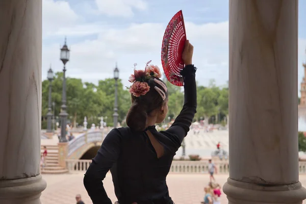 Young teenage woman with black dance dress and pink carnations in her hair, with red fan dancing flamenco. Flamenco concept, dance, art, typical Spanish dance, fan.